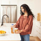 Woman in a kitchen holding a bottle and glass of juice, with a bowl of oranges on the counter.